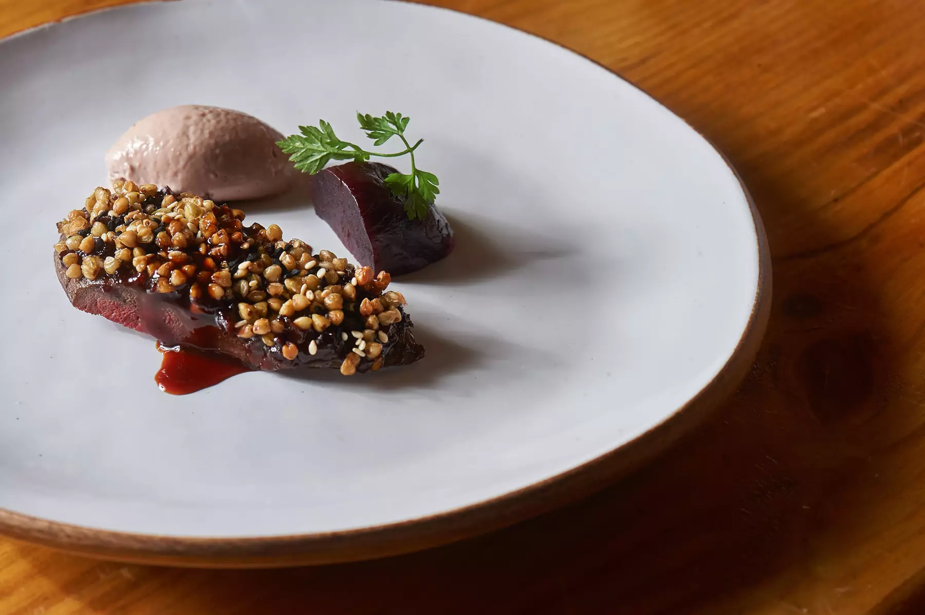 White plate on a wooden surface with a large slice of beetroot with parsley on top, slice of beef with a nut glaze and a spoonful of sauce. Credit Simon Jacobs